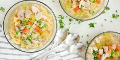 3 glass bowls filled with chicken broth, egg noodles, bite-sized pieces of chicken, carrots and celery garnished with fresh parsley.
